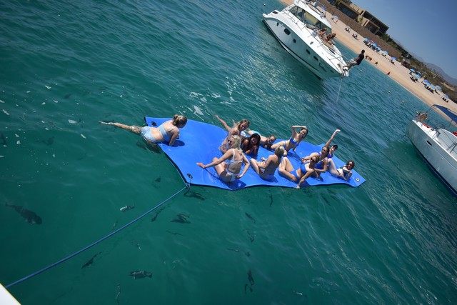 Personas en un tapete flotante junto a un yate en Los Cabos